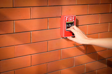 hand of woman is pulling fire alarm on the brick wall