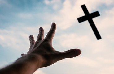 Hand of a man reaching to the cross in the sky.