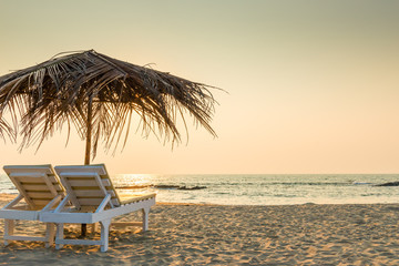 empty chairs under thatched umbrellas on a sandy beach