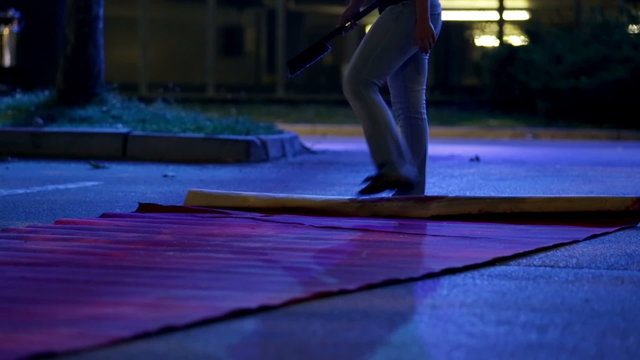 Person kicking and unfolding the red carpet at night