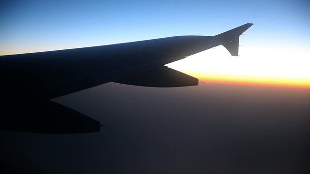 Big airplane wing while flying above clouds at sunrise