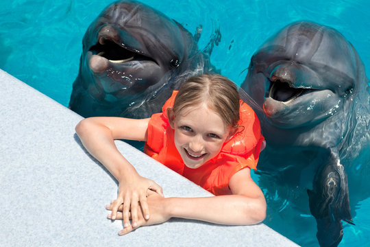 Happy Little Girl Smiling with two Dolphins in Swimming Pool