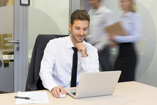 Businessman working in office, business people moving behind him