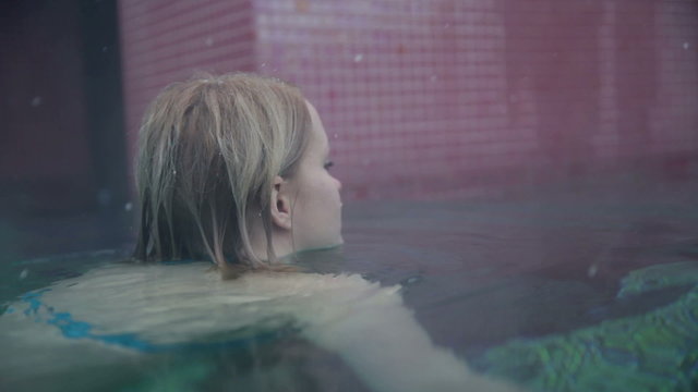 Shot of a pretty young woman in blue bikini that swimms towards the camera, enoying in the outdoor pool when snowing