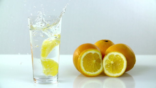Two pieces of lemon fall into glass of water on white background