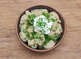 Russian dumplings with dill and sour cream in a clay bowl on a w