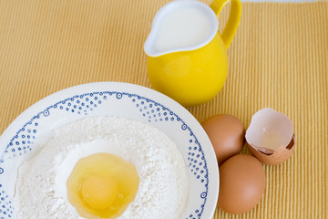 Plate with flour, eggs and milk jug standing