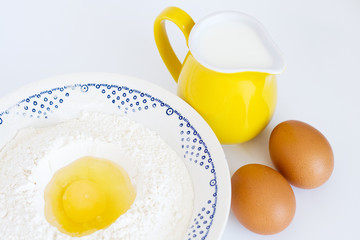 Plate with flour, eggs and milk jug standing on a background