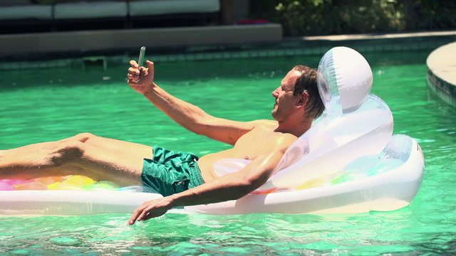 Man taking selfie photo with cellphone lying on air mattress 