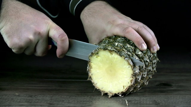 Cutting a slice of pineapple on black background