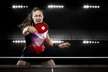Young sports woman tennis-player in play on black background