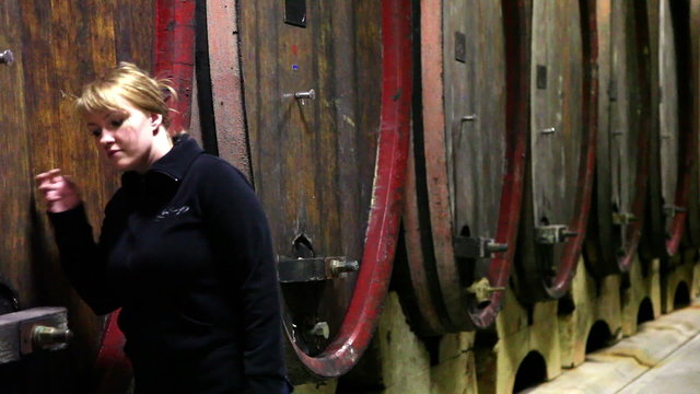 Shot of a women checking the barrels in the wine cellar