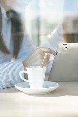 Closeup of coffee cup and girls using a tablet in coffee shop