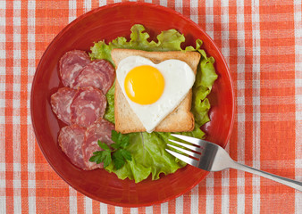 Fried heart-shaped egg on toast with salad and sausage