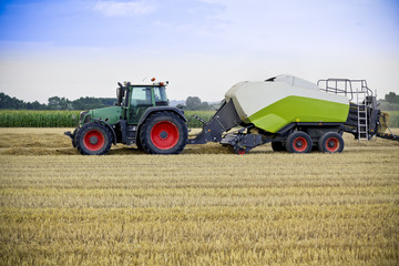 Obraz premium Tractor harvests wheat on a field