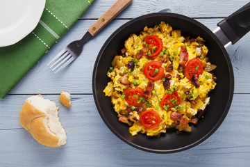 Scrambled eggs in a pan with bacon, onion and tomatoes sprinkled