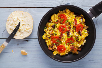 Scrambled eggs in a pan with bacon, onion and tomatoes sprinkled