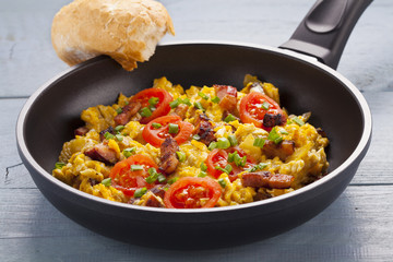 Scrambled eggs in a pan with bacon, onion and tomatoes sprinkled