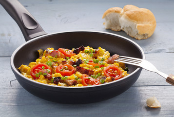 Scrambled eggs in a pan with bacon, onion and tomatoes sprinkled