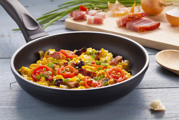 Scrambled eggs in a pan with bacon, onion and tomatoes sprinkled