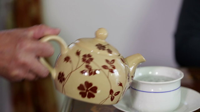 Old lady with shaking hand pouring a tea into a cup 