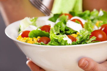 Fit man holding a bowl of fresh salad on grey background