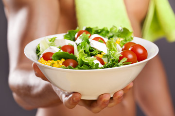 Fit man holding a bowl of fresh salad on grey background