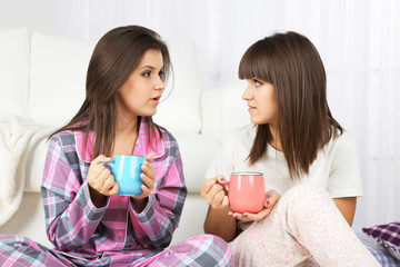 Beautiful girls twins in pajamas drinking tea at home