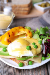 Toast with egg Benedict and avocado on plate on wooden table