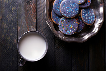 Glazed cookies in metal bowl and mug of milk