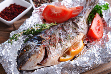 Tasty baked fish in foil on table close-up