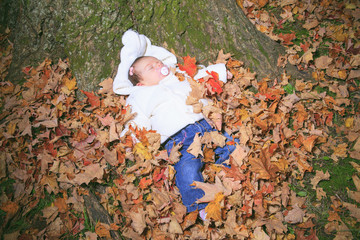 A Newborn baby laying on the leaf of a autumn park
