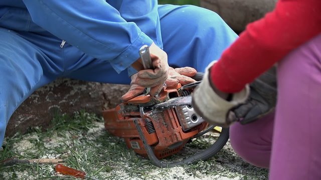 Second person help fix chainsaw holding chain
