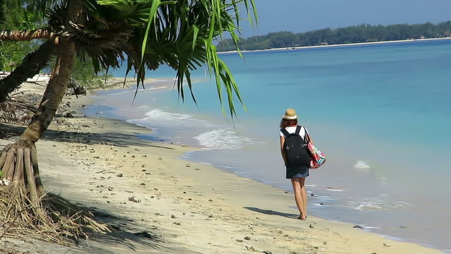 Girl walking down beautiful coastline with backpack and a hat 
