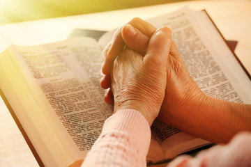 Hands of old woman with Bible on table, close-up