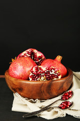 Juicy ripe pomegranates on wooden table, on dark background
