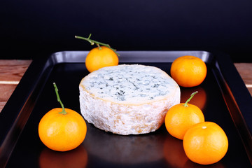 Blue cheese with oranges on metal pan and dark background