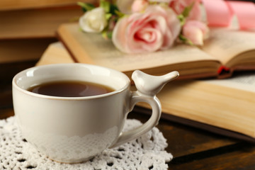 Cup of tea with books and flowers on wooden background