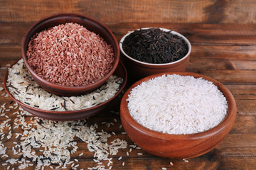 Different kinds of rice in bowls on wooden background