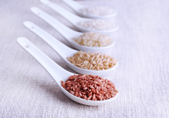 Different types of rice in spoons on fabric background