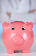 Doctor with pink piggy bank on blue background, close up