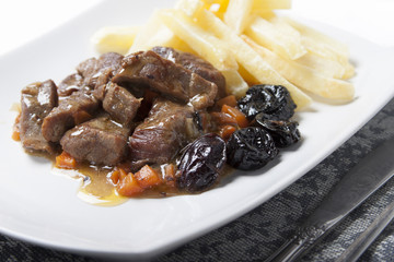 Stew with prunes, carrots and onions garnished with French fries