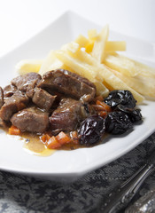 Stew with prunes, carrots and onions garnished with French fries