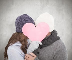 Composite image of couple in warm clothing holding heart