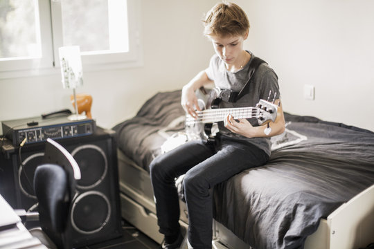 Teen boy playing guitar in bedroom