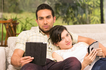 young attractive couple lying in the sofa using their tablets