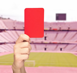 Hand holding a red card in front of a stadium