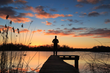 Man on a  jetty enjoying the winter sunset over a lake.