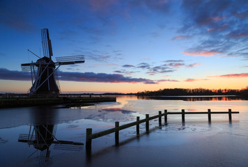 Fototapeta na wymiar Traditional, Dutch windmill at a lake during winter sunset