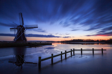 Fototapeta na wymiar Traditional windmill at a lake during a cold sunset in winter.